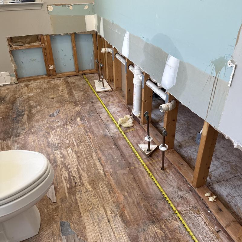 Bathroom plumbing and damaged subfloor exposed for repair