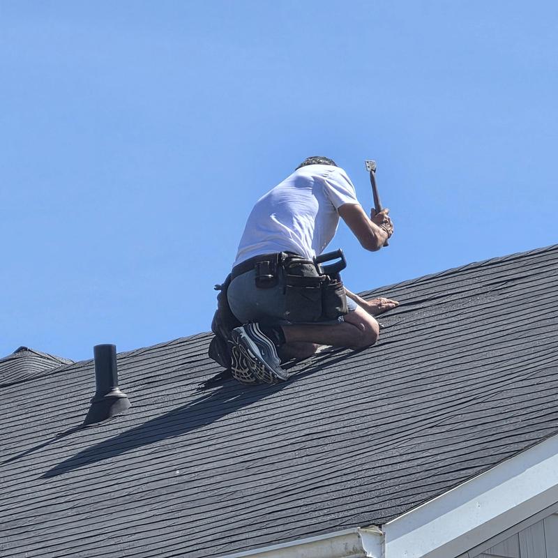 Asphalt shingles roof with worker inspecting damage