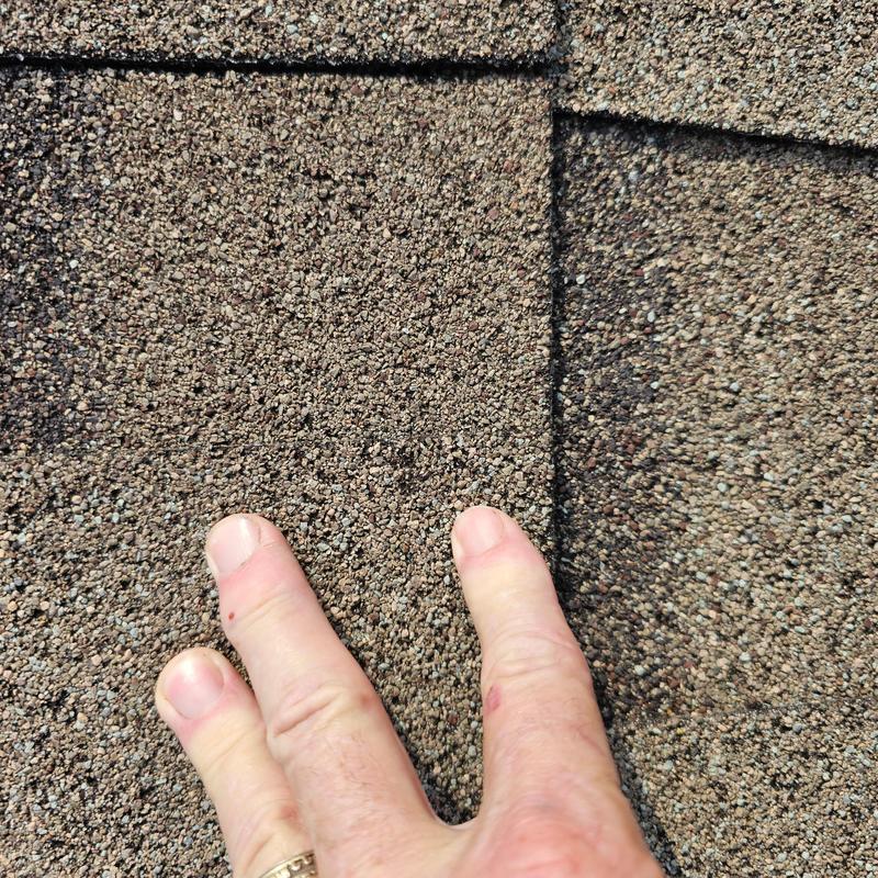 Asphalt roof shingles close-up with hail damage and hand