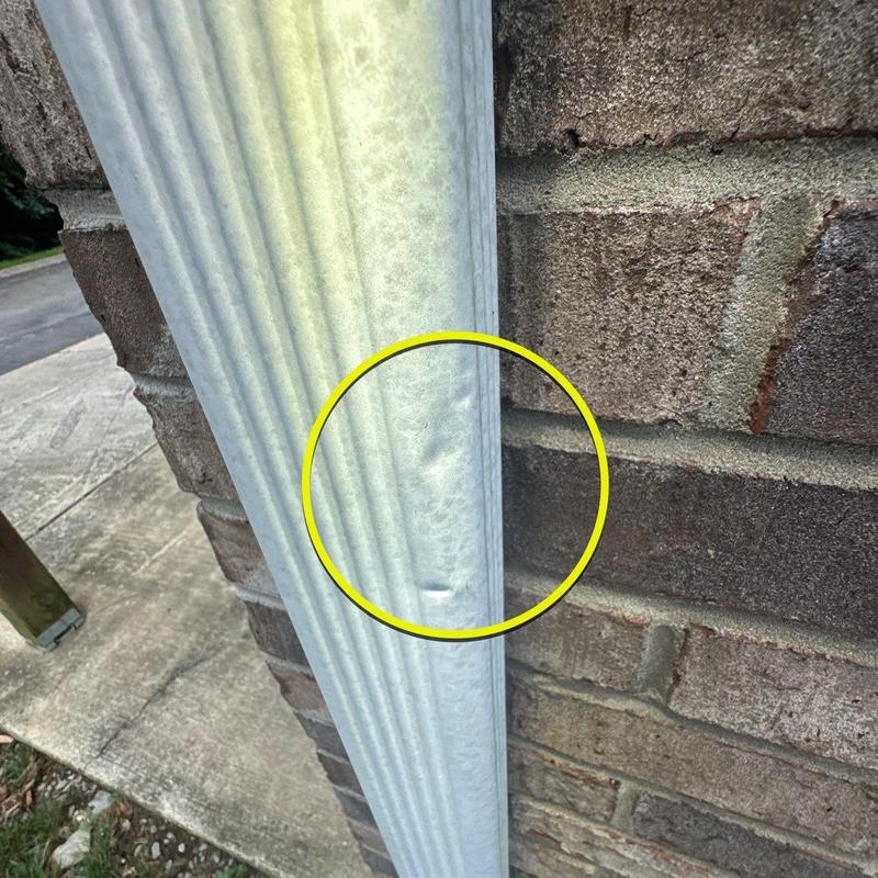 Downspout dent with minor hail damage near brick wall