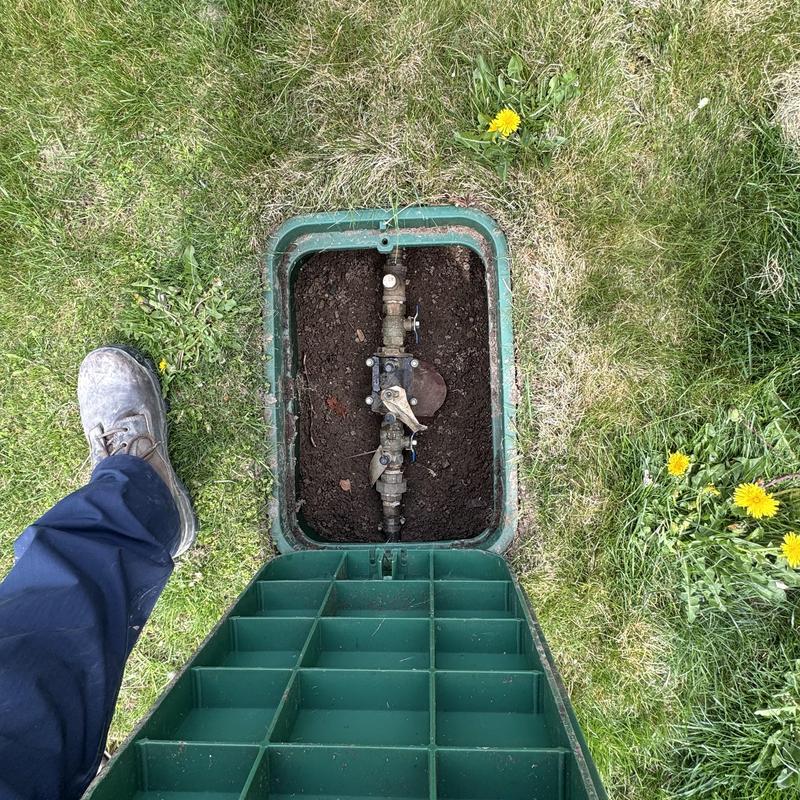 Water main valve box open in grassy yard with worker boot Water main valve box open in grassy yard with worker boot