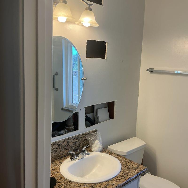 Bathroom wall plumbing access cutouts behind sink and mirror