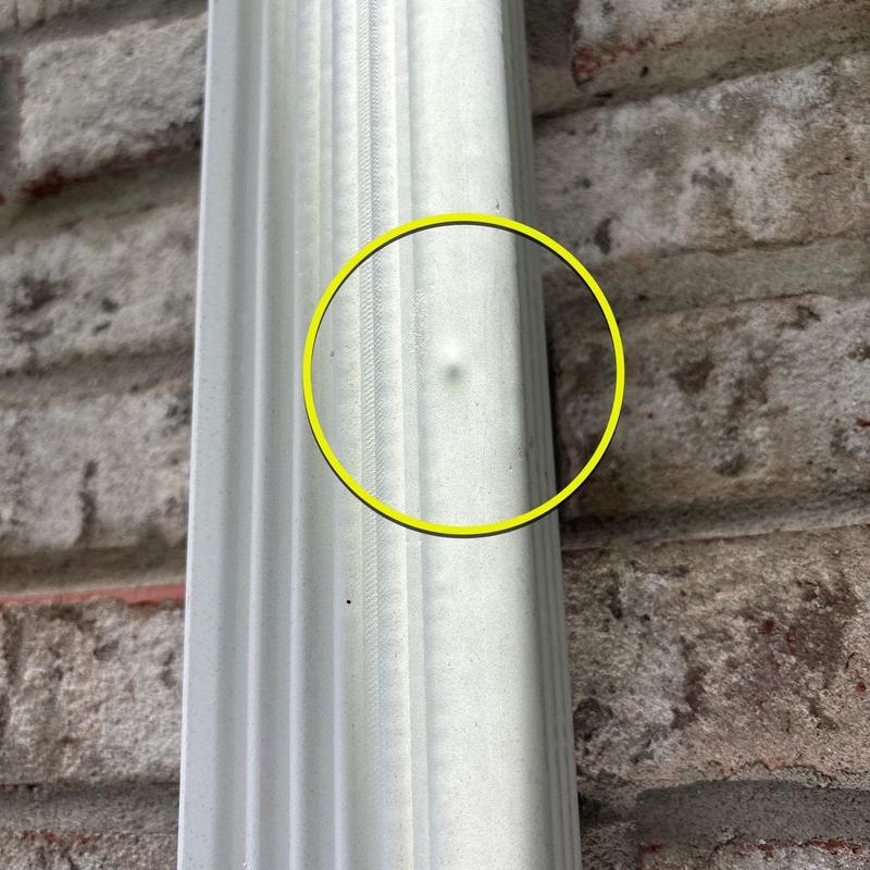 Aluminum downspout dent damage on exterior wall