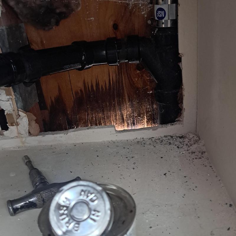 Sink drain pipe section inside wall with tool nearby