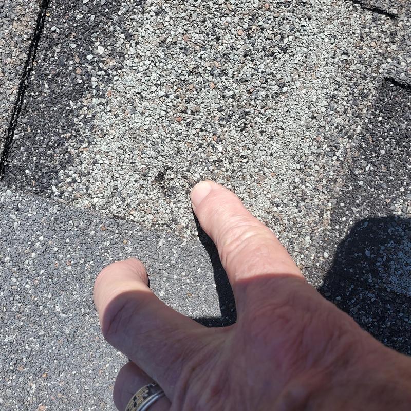 Roof shingle hail damage close-up with hand pointing