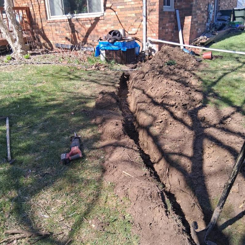 Sump line trench excavation beside brick house exterior