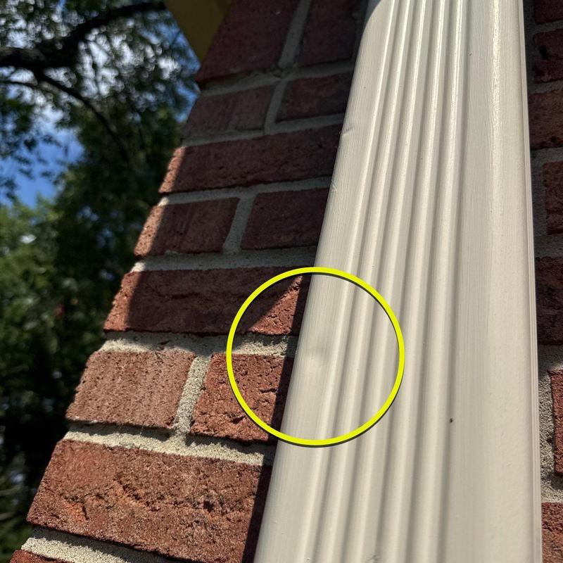 Vinyl downspout dent damage on brick wall exterior