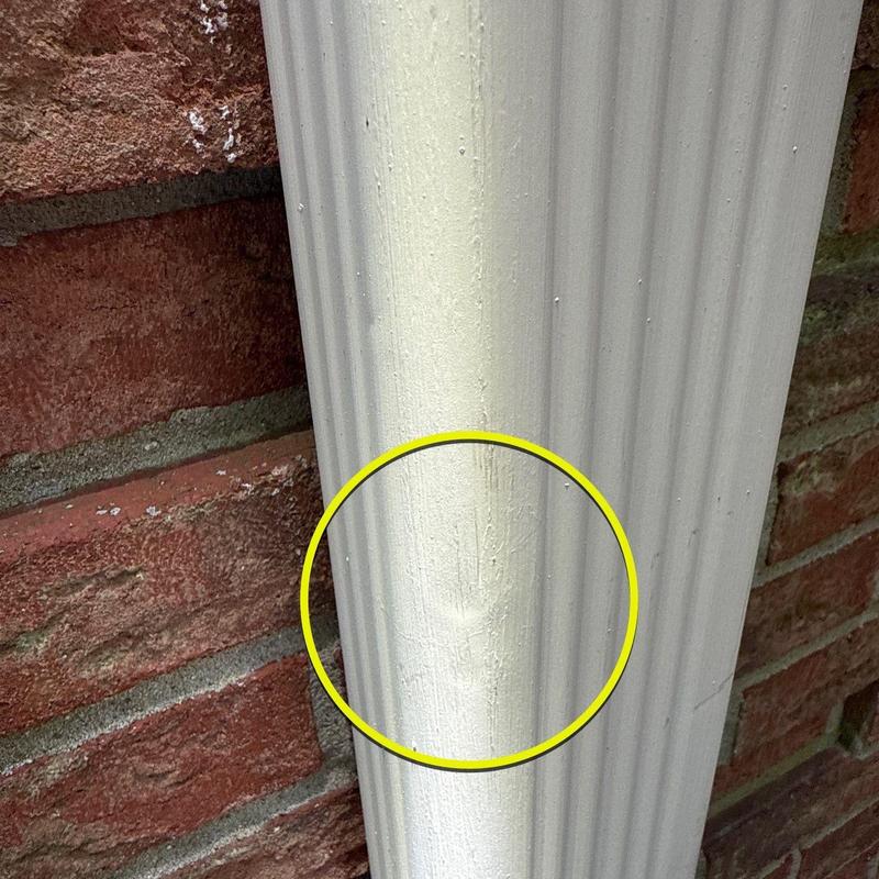 Downspout dent damage on white exterior gutter system
