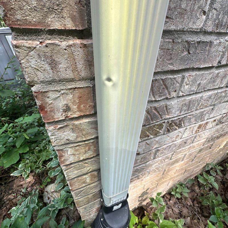 Downspout with dent near brick wall corner outdoors