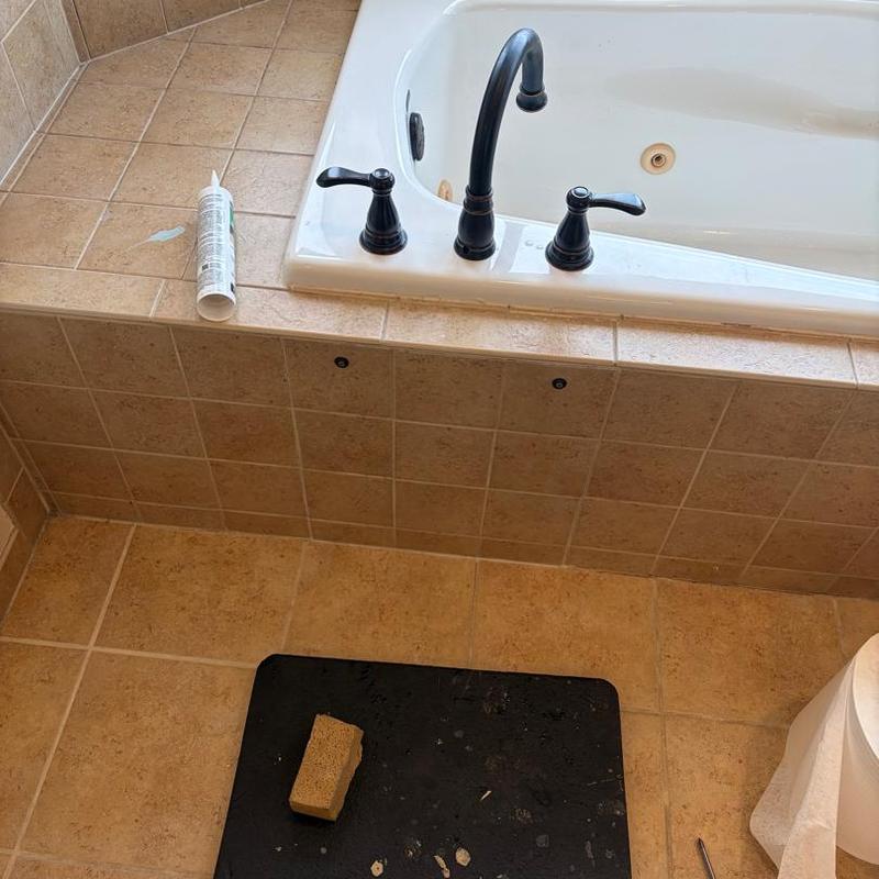 Bathtub faucet installation with caulking and tools nearby