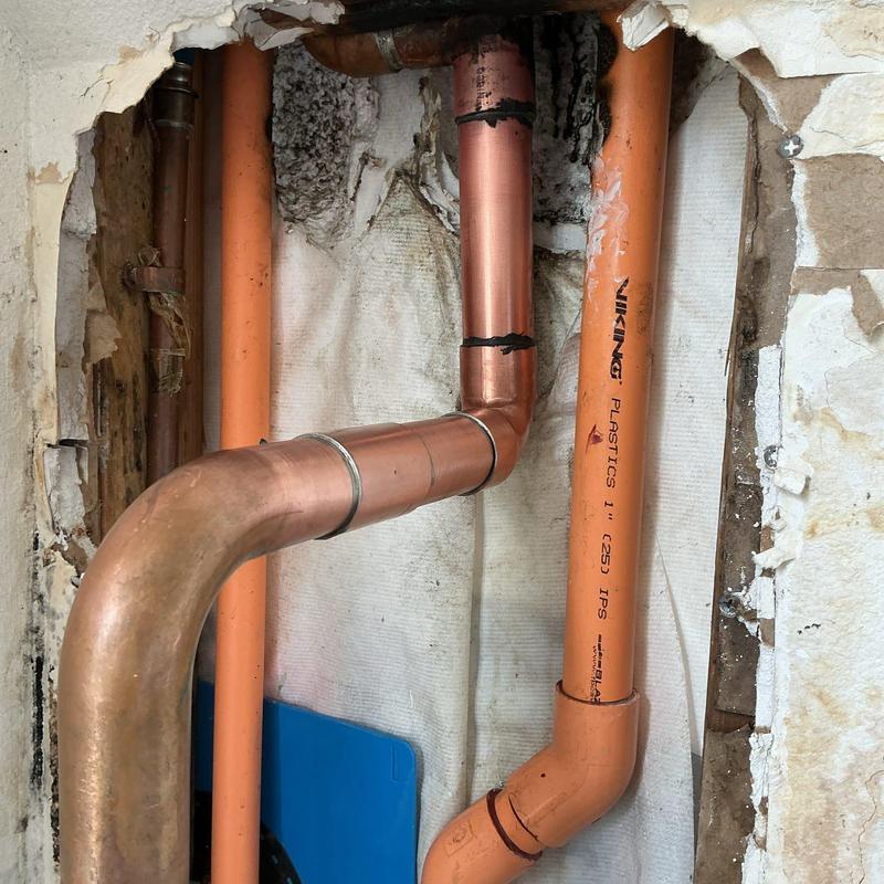 Copper pipe and orange PVC pipe plumbing installation detail
