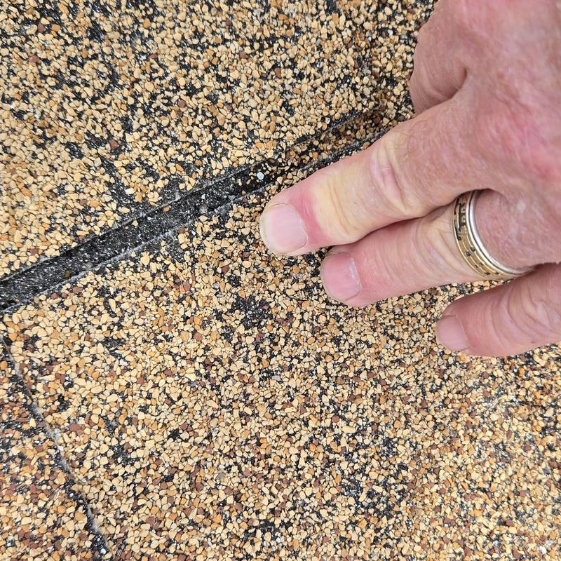 Asphalt shingle hail damage close-up with hand for scale