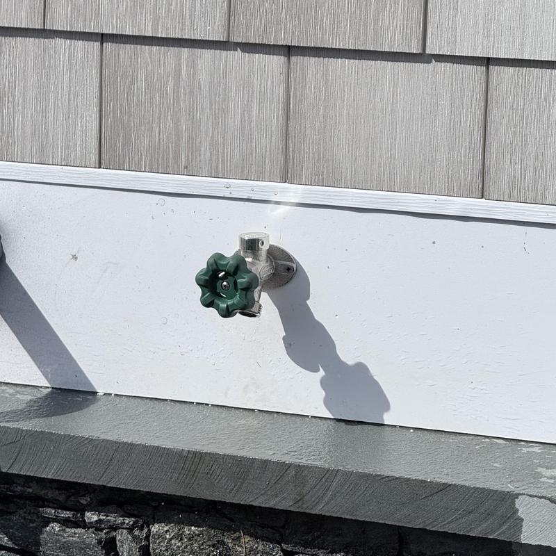 Silcock valve with green handle on house exterior wall