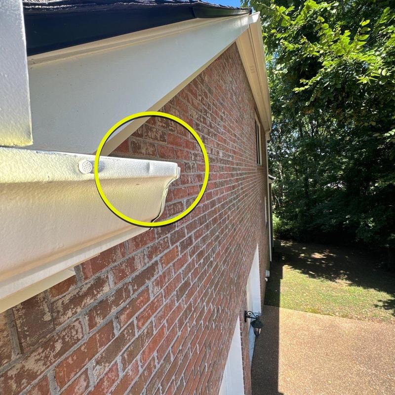 Gutter end cap with minor dent highlighted on brick wall