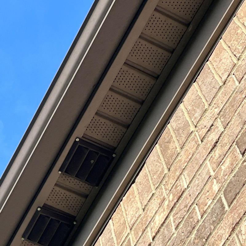 Roof soffit vents and brick siding under clear sky