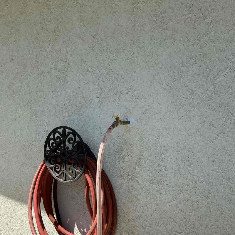 Hose bib with attached red garden hose reel and hose