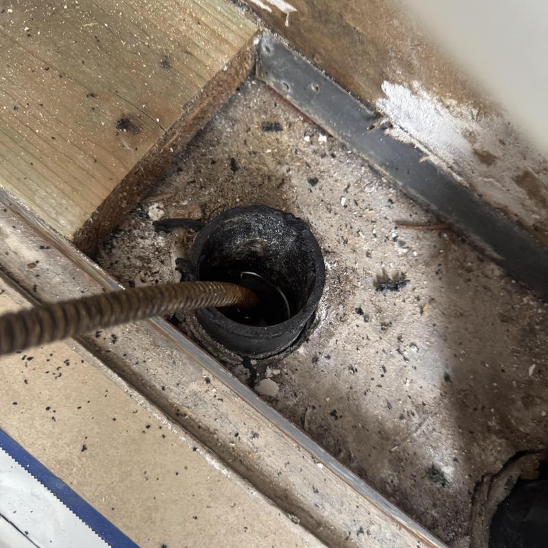 Sewer line drain with cleaning snake inside drywall floor cavity