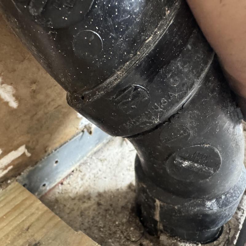 Sewer drain pipe with visible crack behind drywall