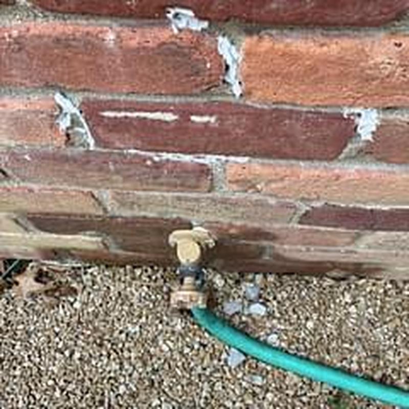 Hose bib with green garden hose attached on brick wall