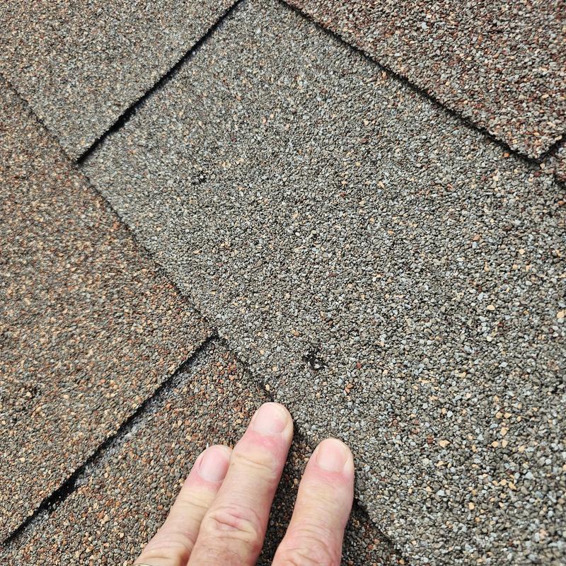 Asphalt roof shingles with hail damage and hand for scale