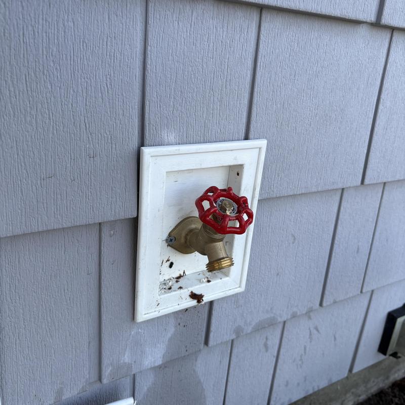 Outside faucet with red valve handle on gray siding