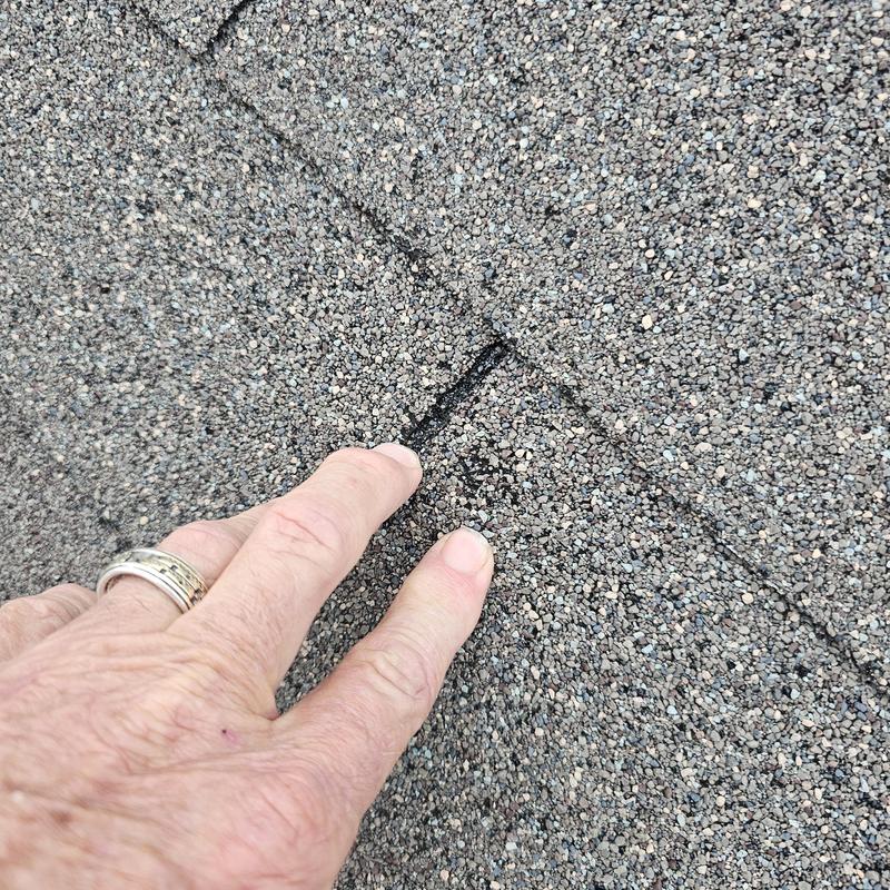 Asphalt roof shingle damage close-up with finger pointing