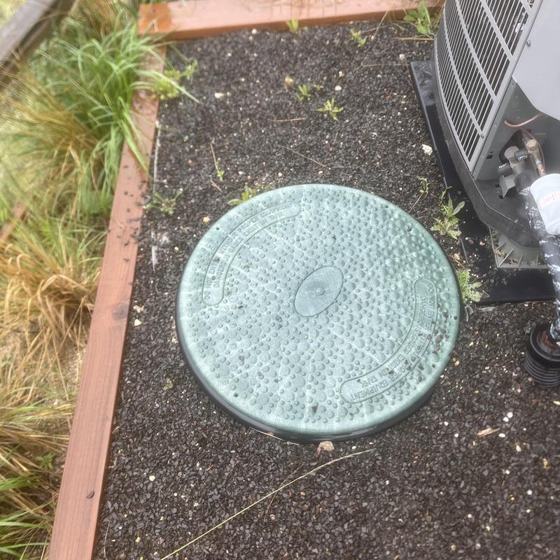 Septic tank cover near HVAC unit on gravel bed