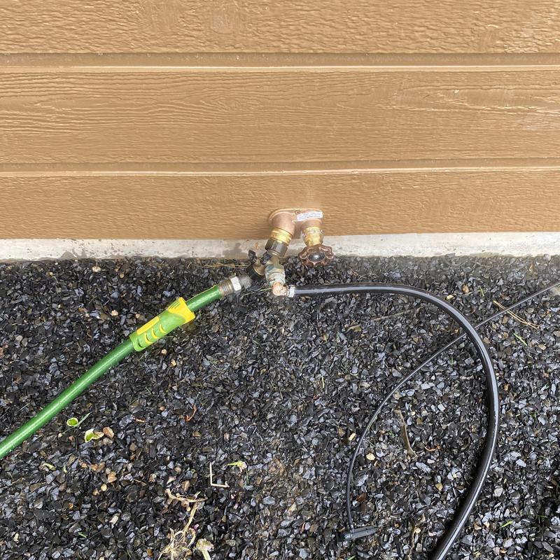 Hose bibb with attached garden hose on gravel ground