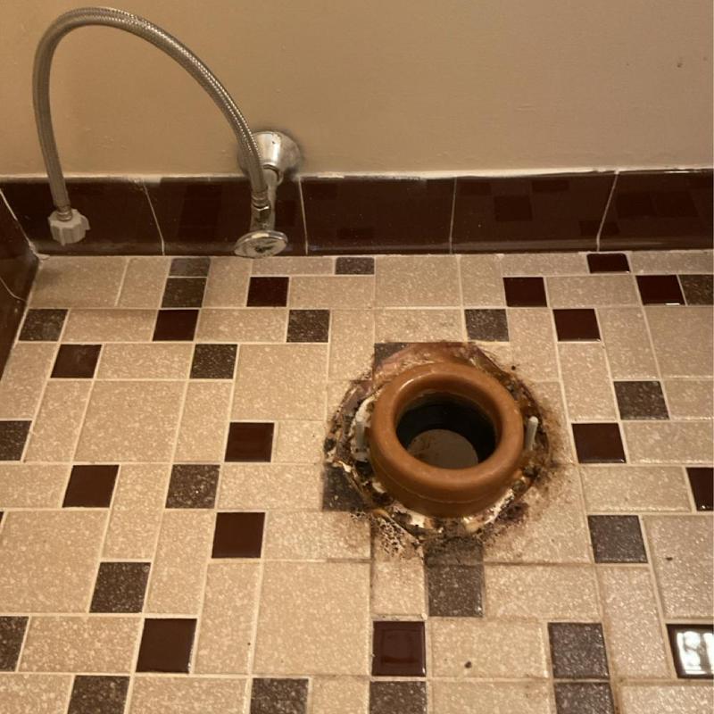 Toilet flange on tiled bathroom floor with water supply line