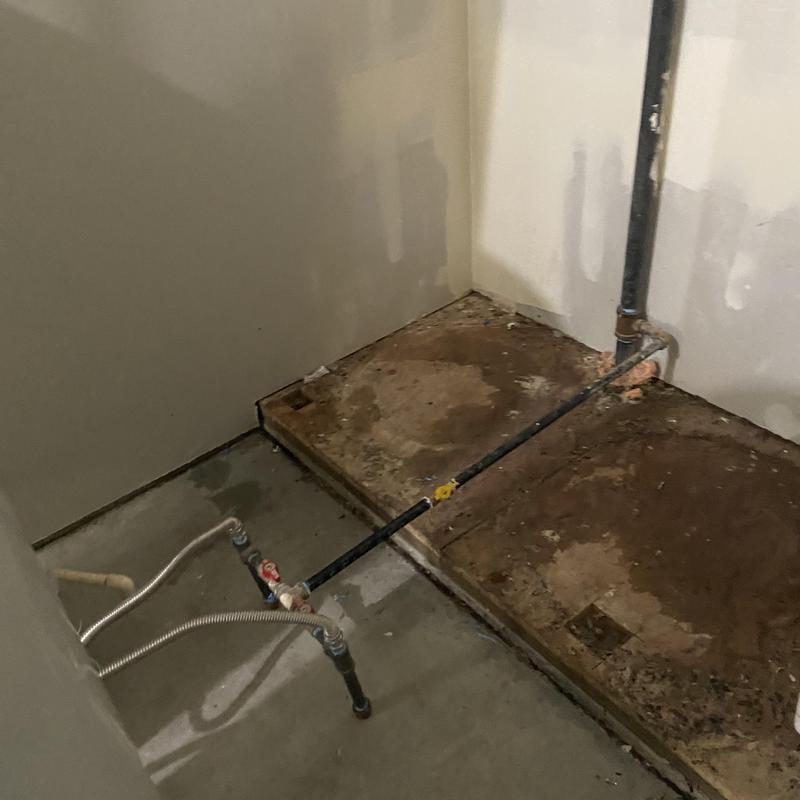 Water heater base and plumbing after removal in utility room