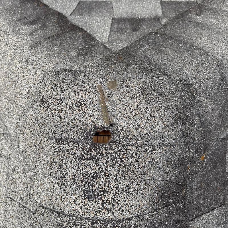 Roof shingle with hole and hail damage close-up