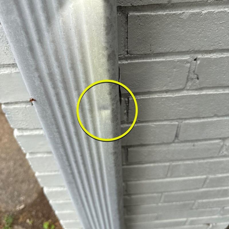 Metal downspout dent with minor hail damage on brick wall