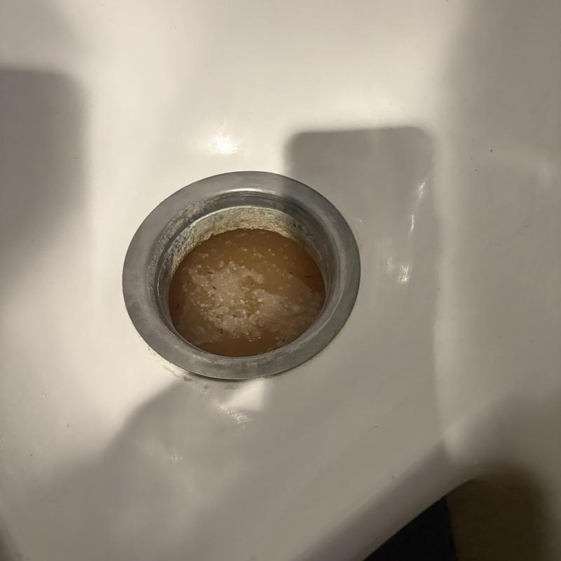 Clogged commercial urinal drain with buildup and corrosion