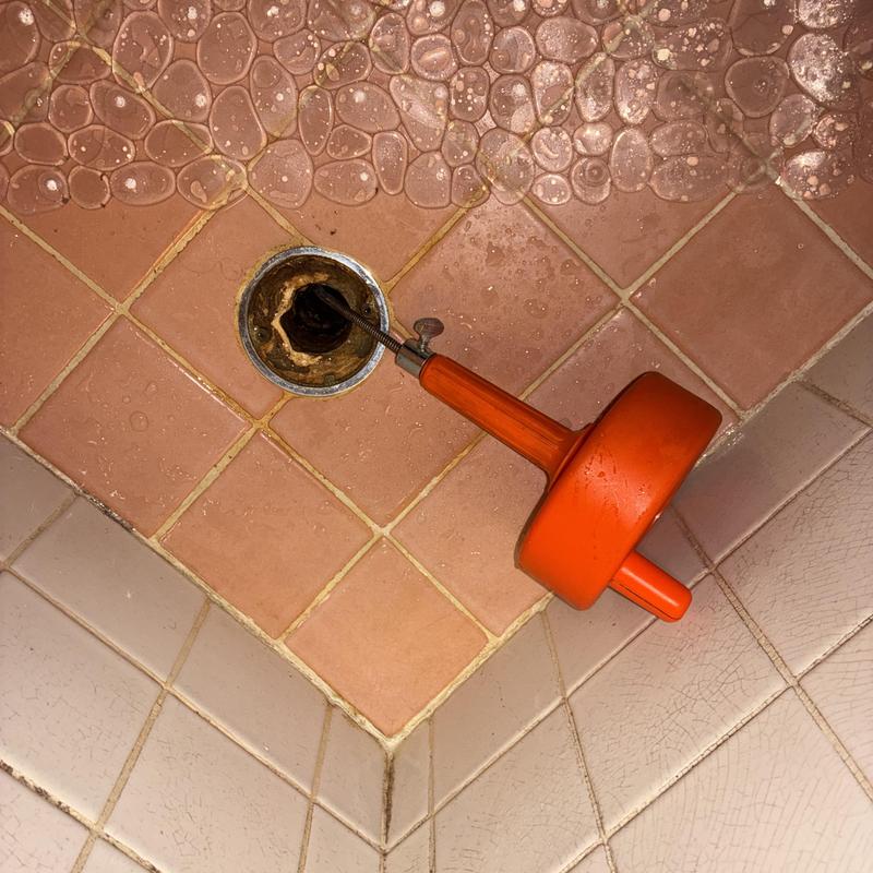 Shower drain clearing tool inserted in tiled floor drain