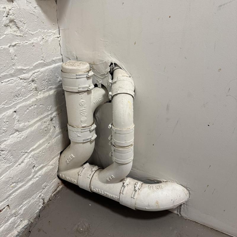 PVC drain vent pipe with wall mounting in basement corner