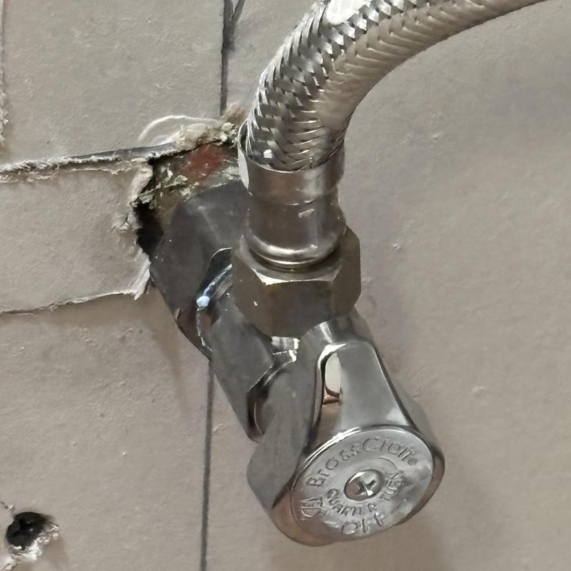 Angle stop valve with braided supply line on tiled wall