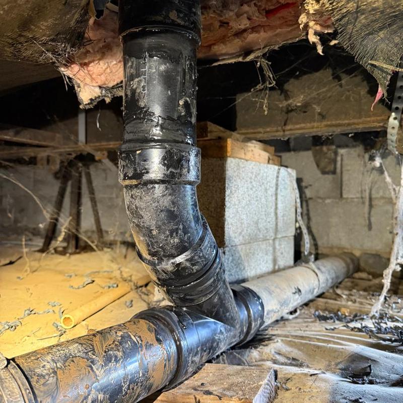 Black PVC drain pipe with fitting replacement in crawl space