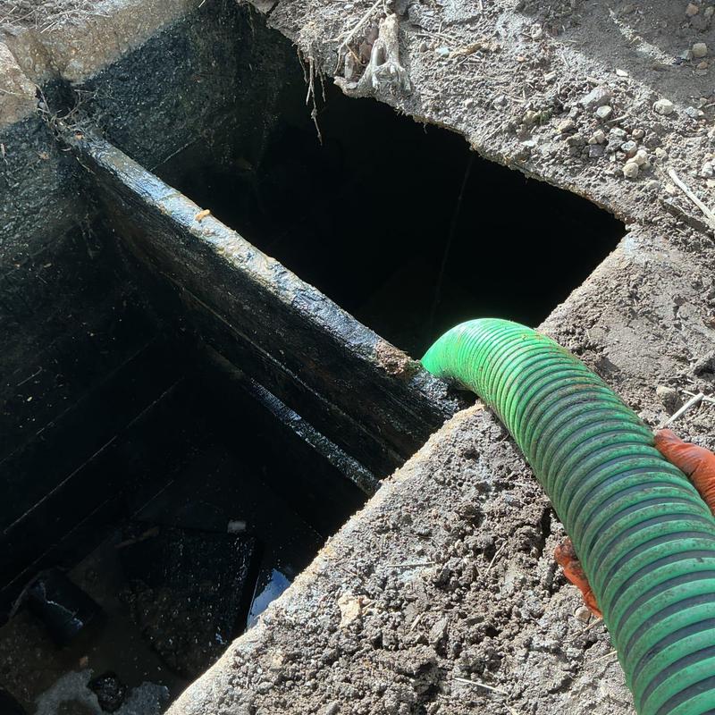 Septic tank pump-out with green hose at excavation site