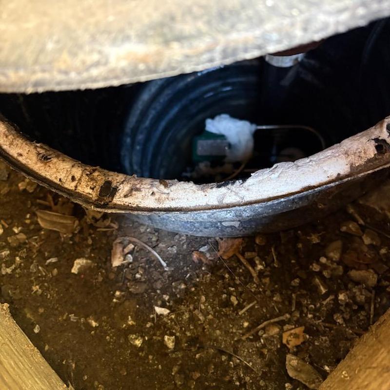 Sump pump basin opening with exposed soil and debris