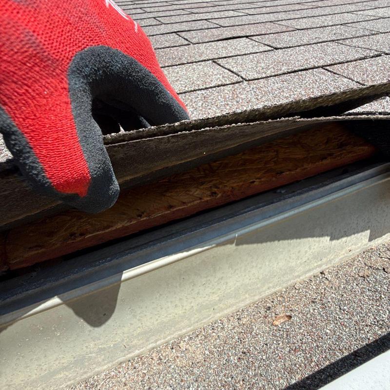 Roof shingles lifted to inspect damage near gutter edge
