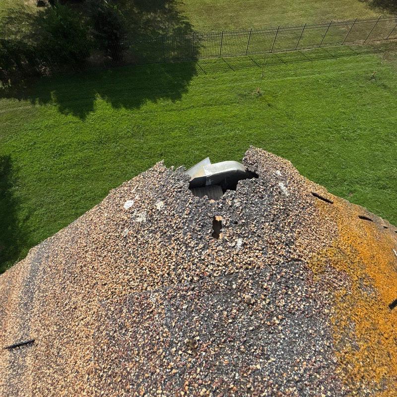 Shingles with large hole and visible damage on roof peak