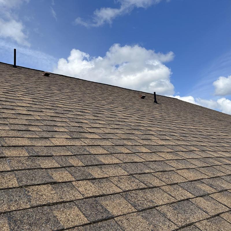 Architectural shingle roof with vent pipes under blue sky