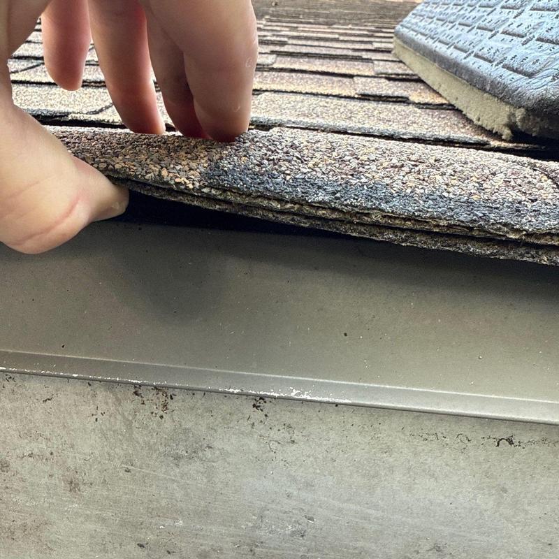 Asphalt shingles lifted to inspect metal flashing underlayment