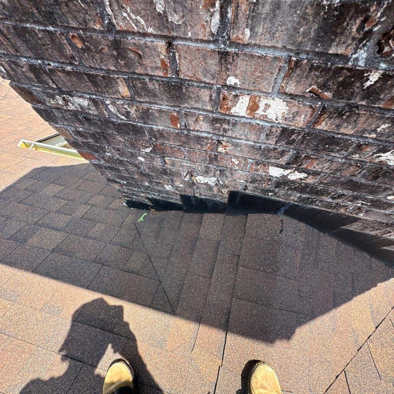 Asphalt shingles near brick chimney with wear marks