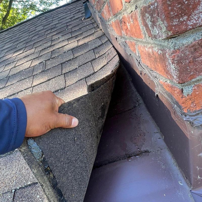 Roof shingles lifted near brick chimney flashing inspection