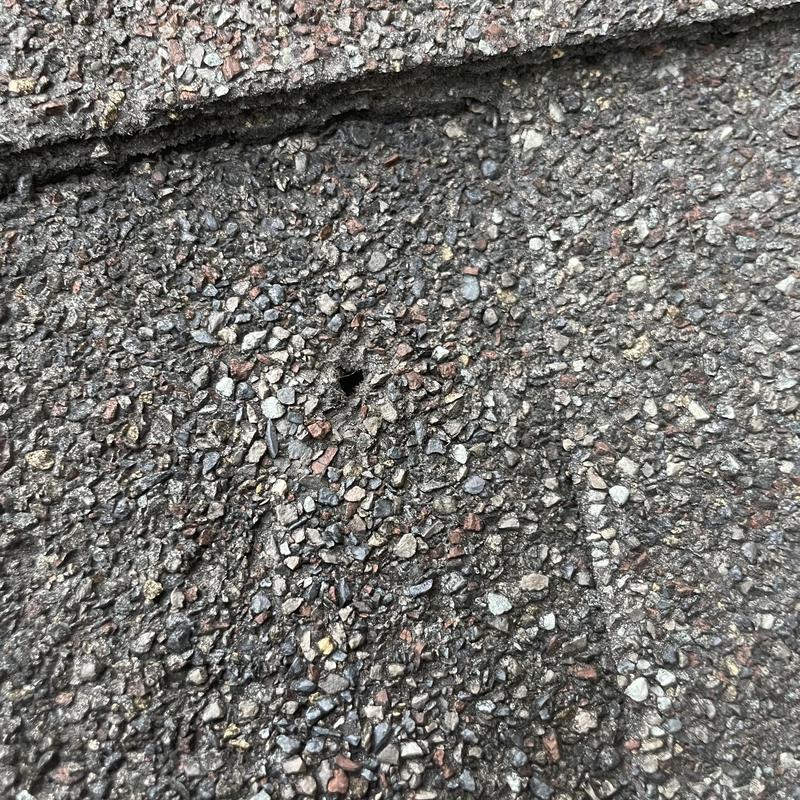 Asphalt shingle with nail hole and granule loss close-up Asphalt shingle with nail hole and granule loss close-up