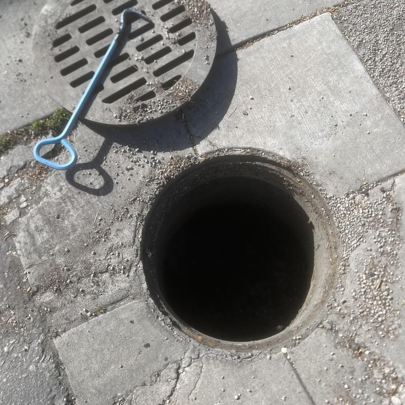 Storm water basin open with cover and tool nearby