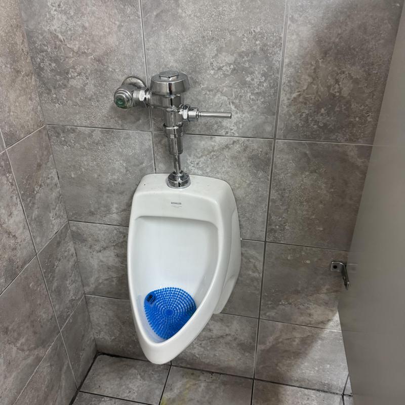 Urinal with flush valve and blue urinal mat Urinal with flush valve and blue urinal mat