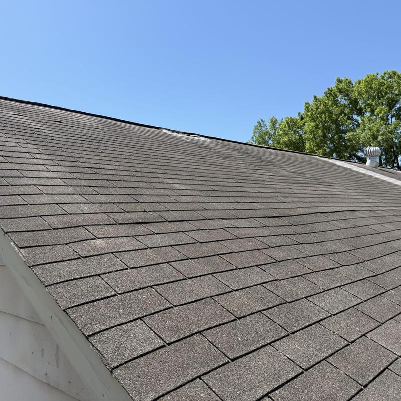 Asphalt shingle roof showing significant wear under clear sky