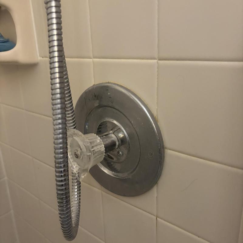 Shower handle and flange with attached hose in tiled wall